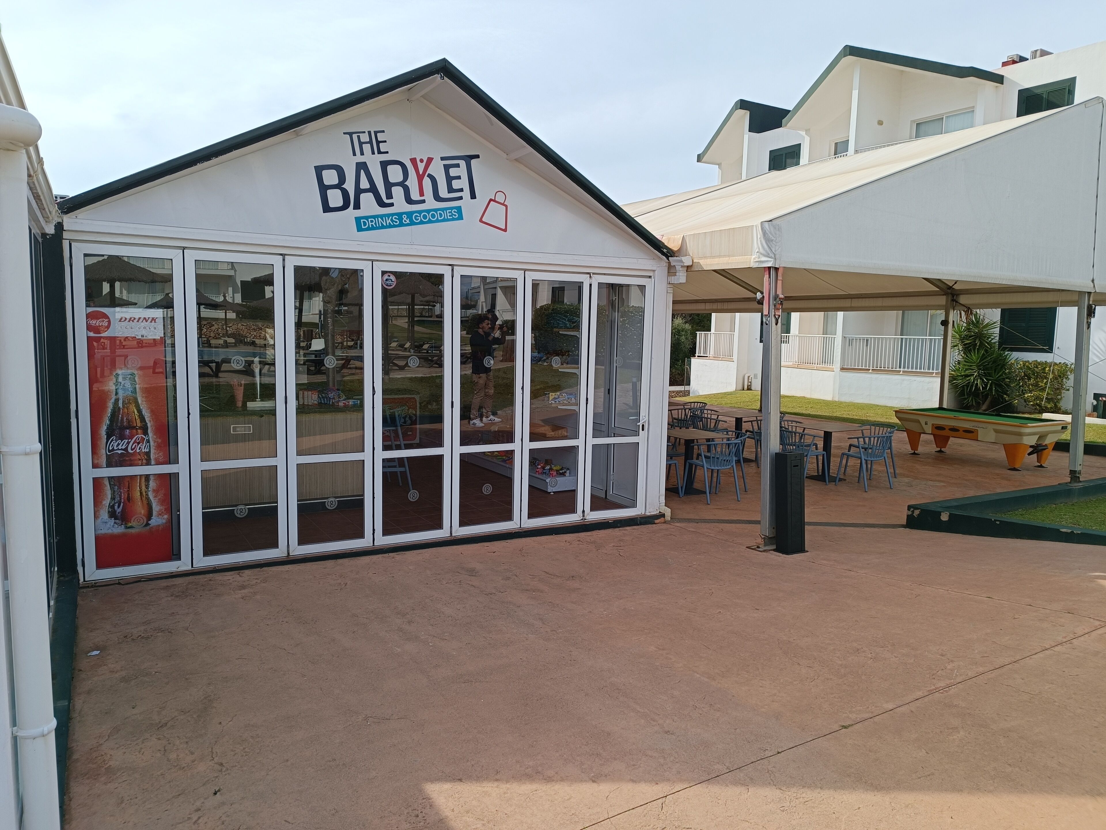 Une devanture de magasin appelée «The Baryet», avec une publicité pour Coca-Cola, un espace extérieur abrité avec des tables et un billard.