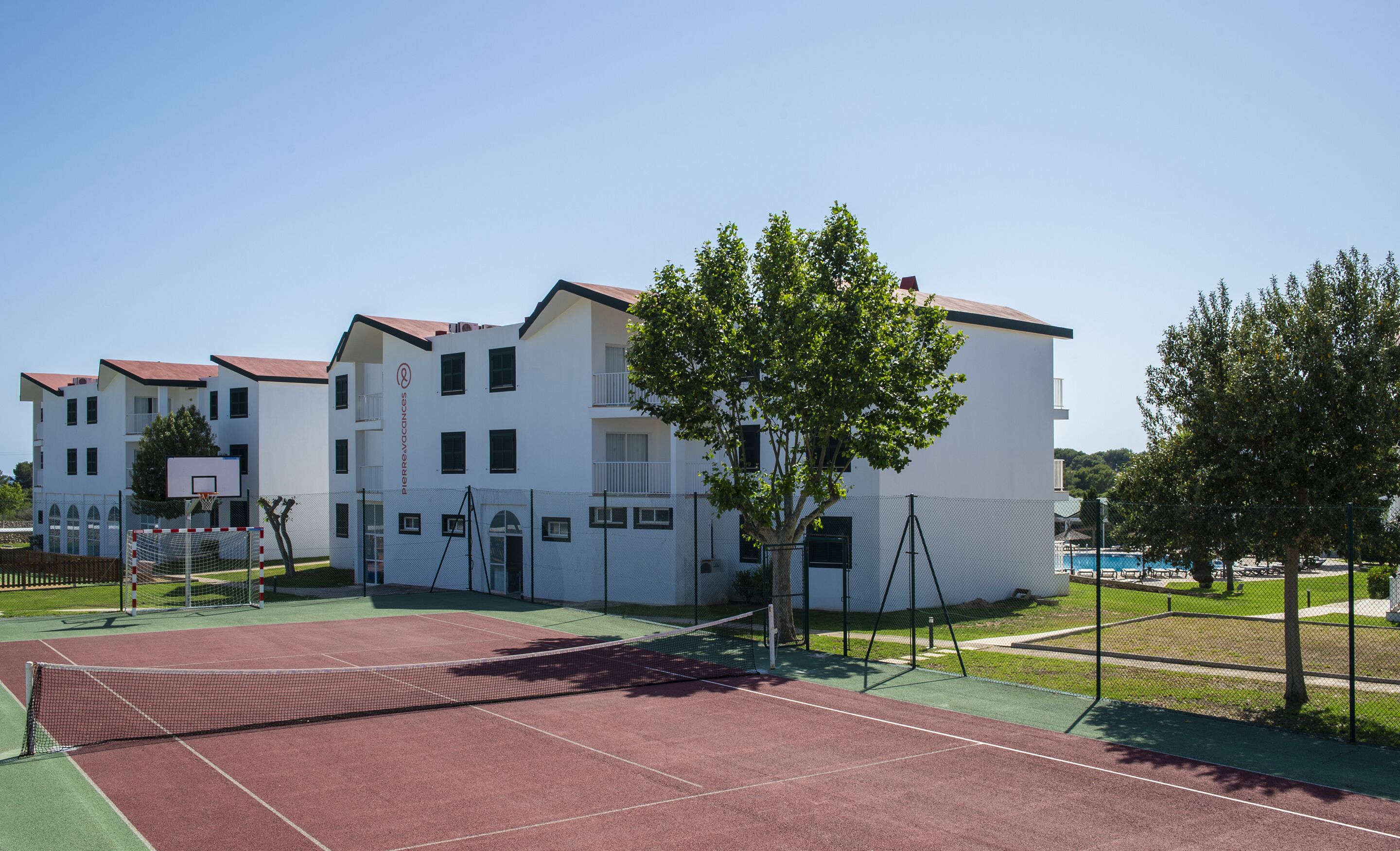 A multi-story building with a tennis court in front.