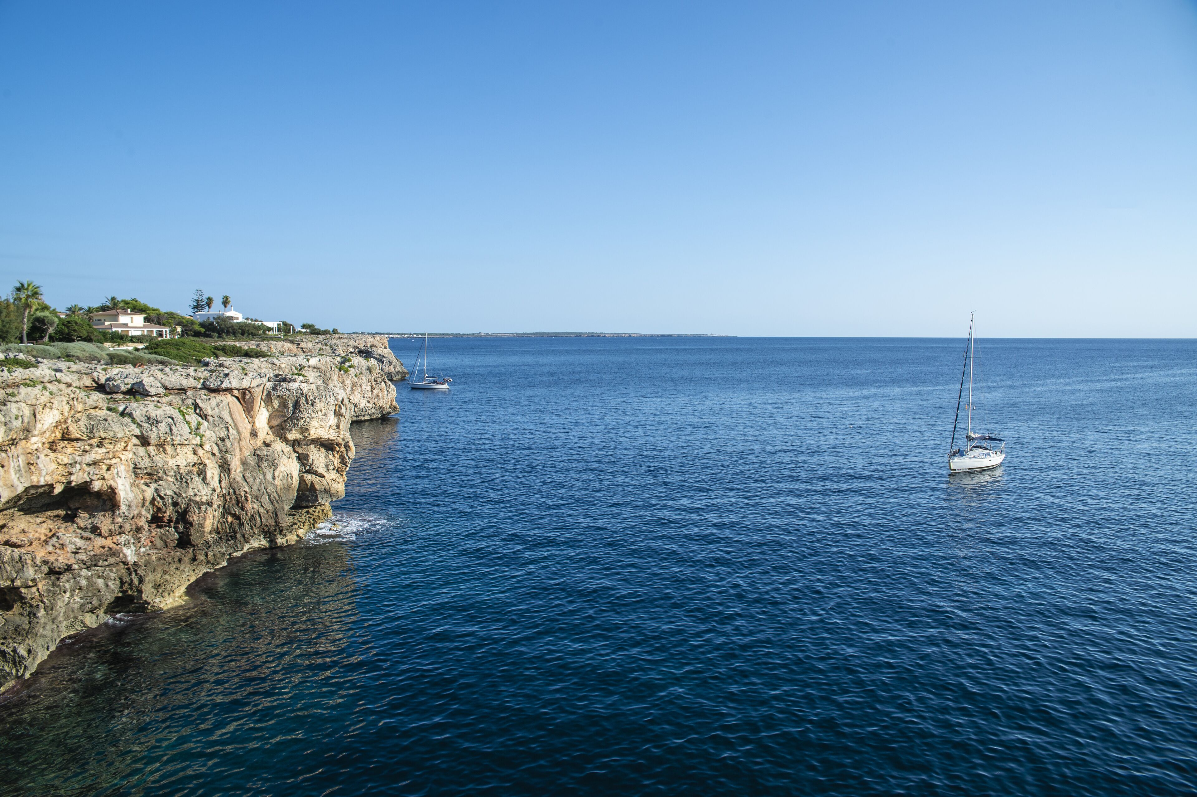Paesaggio costiero con una scogliera rocciosa, una barca a vela e una costa in lontananza.