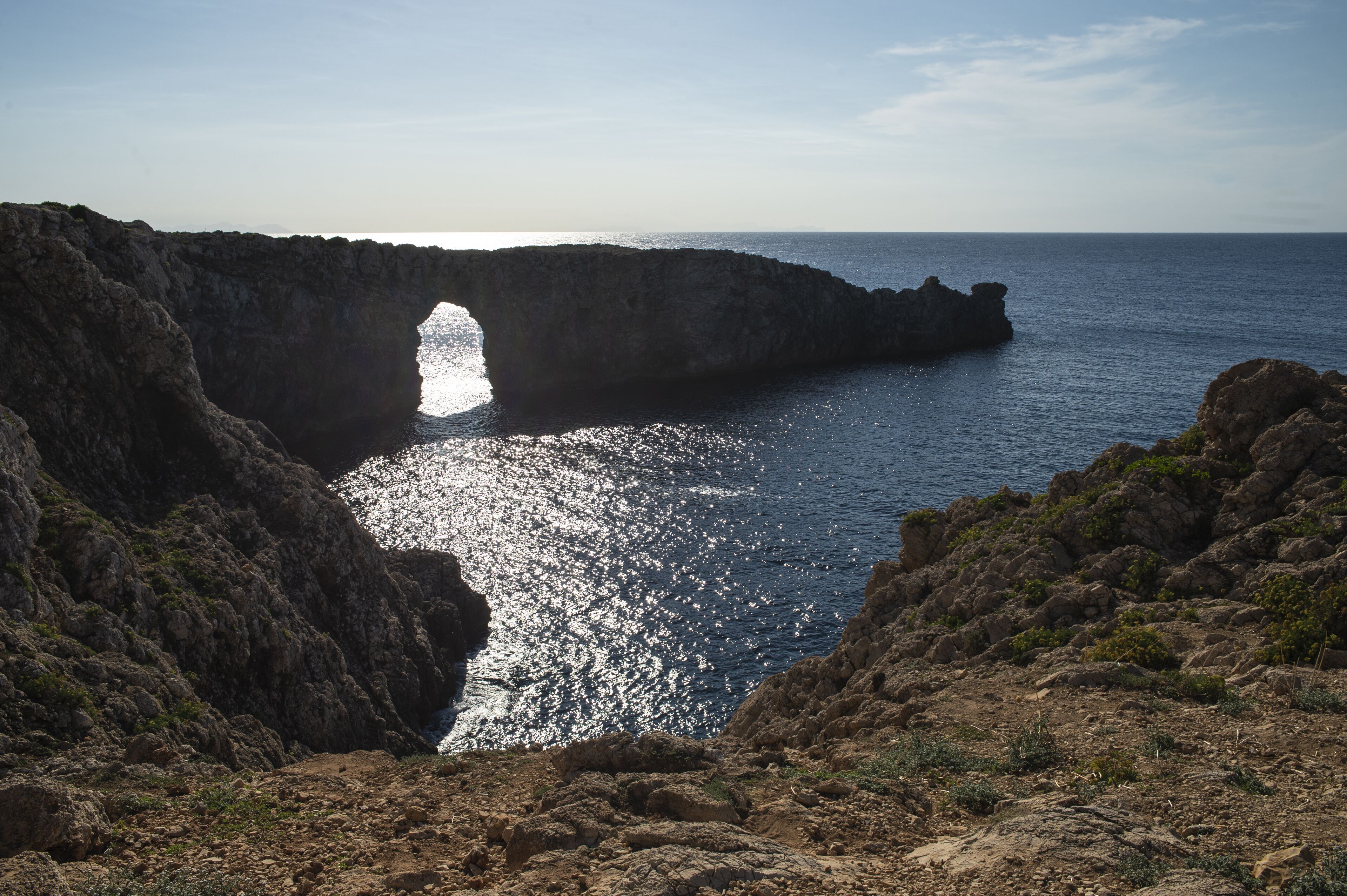 A coastal landscape with a natural rock formation and a clear view of the sea.