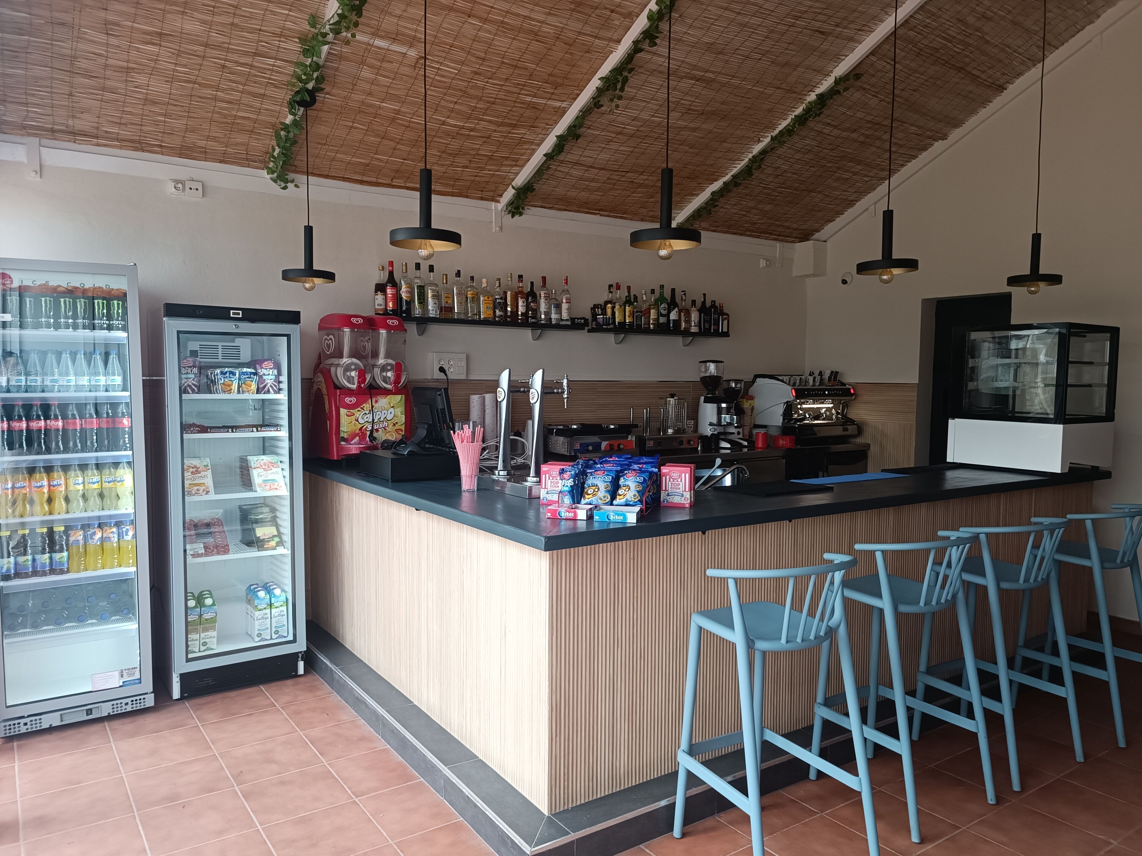 A bar area with a counter, seating, a beverage dispenser, and a refrigerated display.