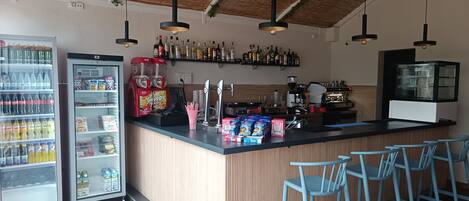 A bar area with a counter, seating, a beverage dispenser, and a refrigerated display.