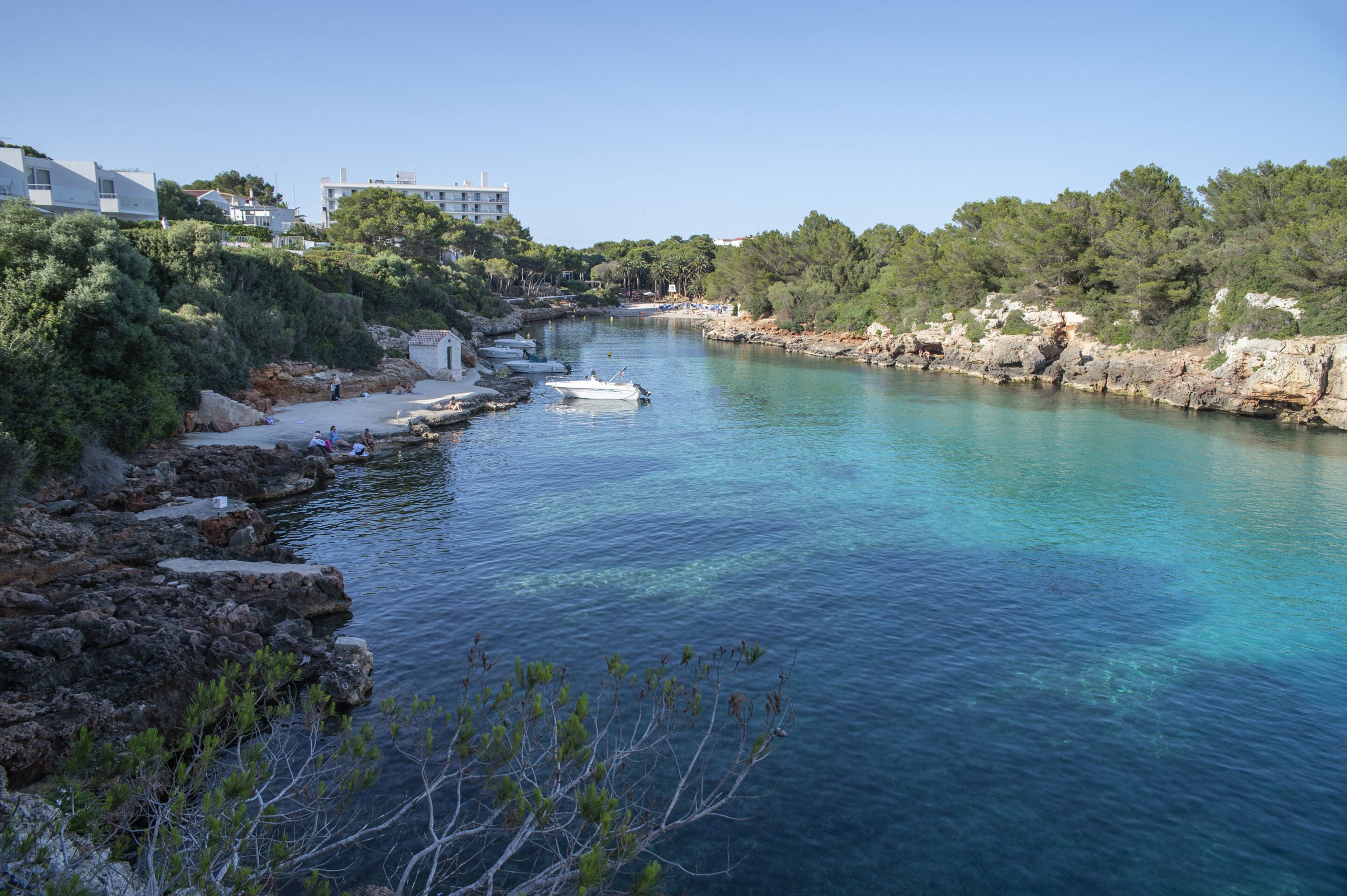 Eine Küstenlandschaft mit klarem, blauem Wasser, felsigen Ufern und Gebäuden im Hintergrund.