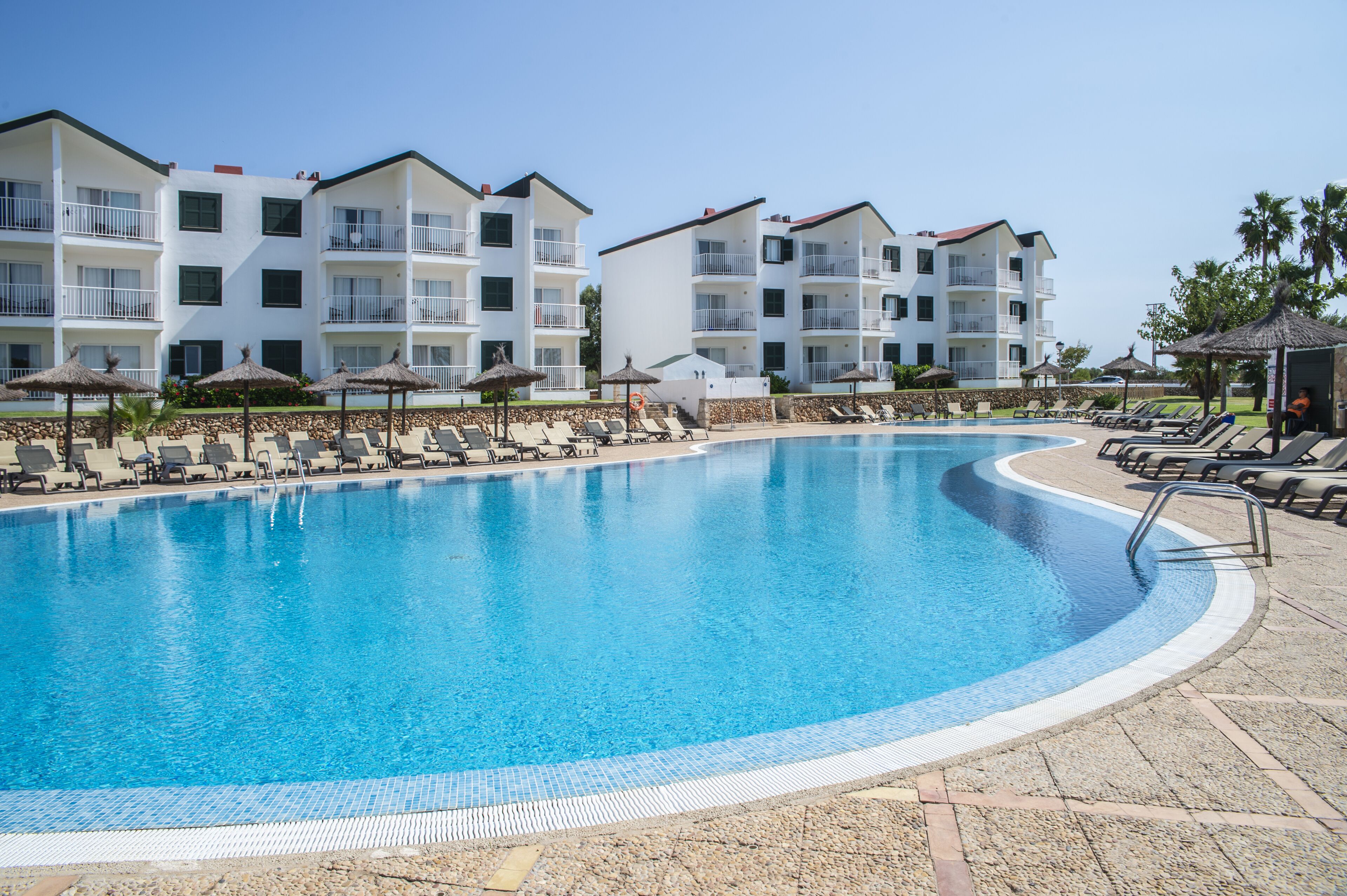 A swimming pool with lounge chairs and umbrellas, surrounded by multi-story buildings with balconies.