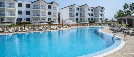 A swimming pool with lounge chairs and umbrellas, surrounded by multi-story buildings with balconies.