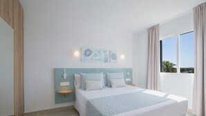 A bedroom with a bed, two wall-mounted nightstands, a headboard, and a window with curtains. - Pierre & Vacances Menorca Cala Blanes (Ciutadella de Menorca)