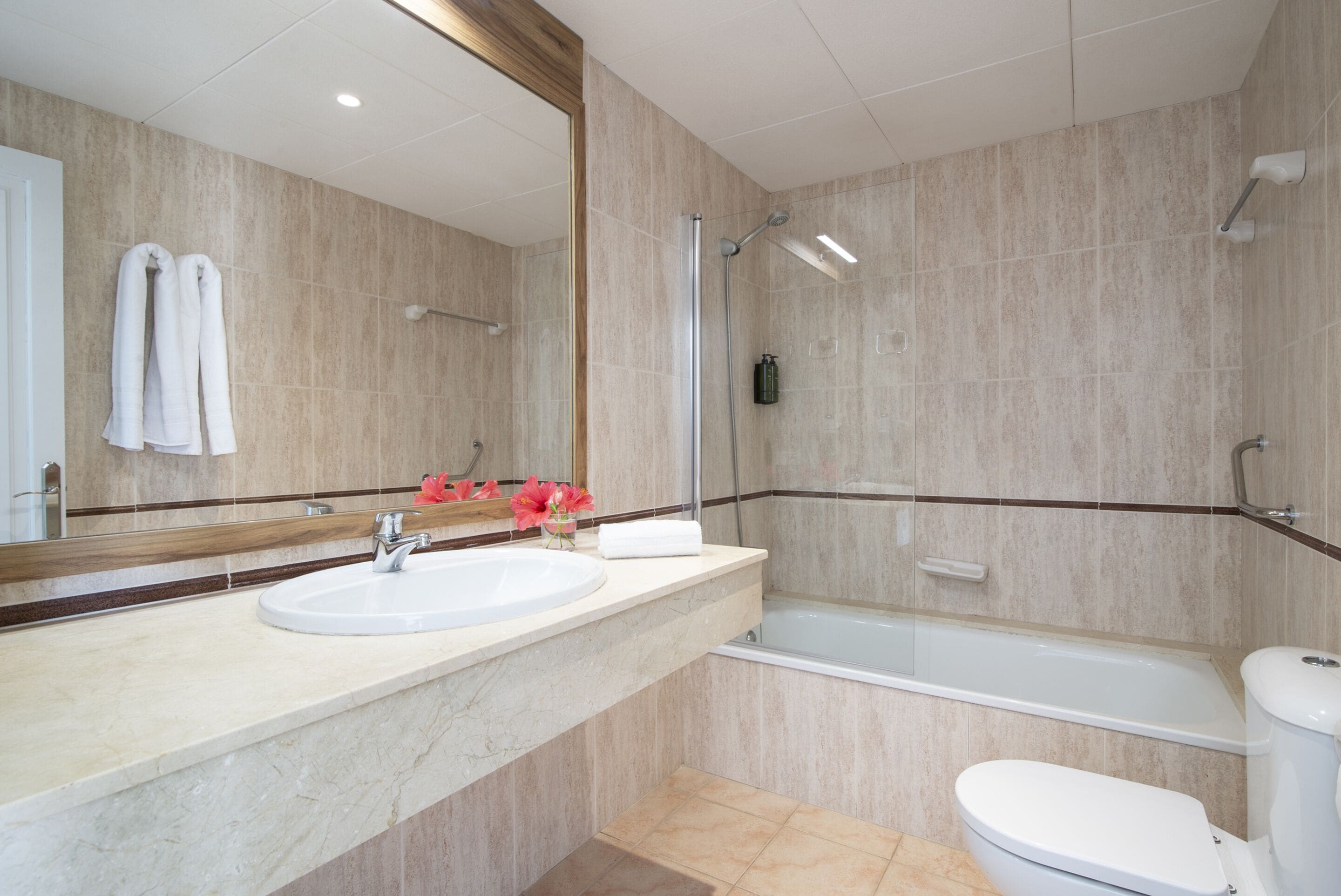 A modern bathroom with a marble sink, a large mirror, a bathtub, and a toilet.