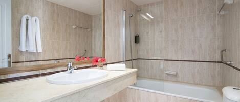 A modern bathroom with a marble sink, a large mirror, a bathtub, and a toilet.