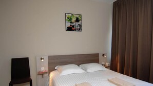 Quarto de hotel com cama, duas almofadas, uma cadeira, mesa de cabeceira com abajur e uma obra de arte na parede.