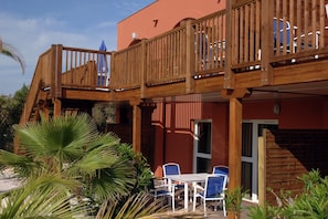 Eine Holzdar Terrasse mit Balkon, Sitzgelegenheiten im Freien und einem Gebäude mit der Nummer 7.