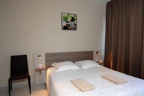 Une chambre d’hôtel comprenant un lit, deux oreillers, une chaise, une table de chevet avec une lampe et une œuvre d’art murale.