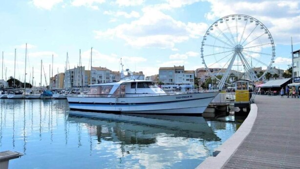 Ein Yachthafen mit vertäuten Booten, ein Riesenrad im Hintergrund und eine Promenade mit Geschäften.