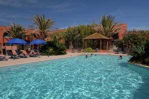 A swimming pool with clear water, surrounded by lounge chairs and umbrellas, and palm trees.