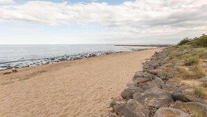A sandy beach with a rocky shoreline and a distant pier. - Relaxed Beachside Living (LE CAP D'AGDE)