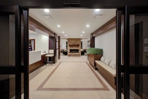 Un vestíbulo de hotel con chimenea central, zonas de estar y una recepción.
