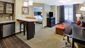 Een hotelkamer met kitchenette, eethoek, bank, televisie en badkamer.
