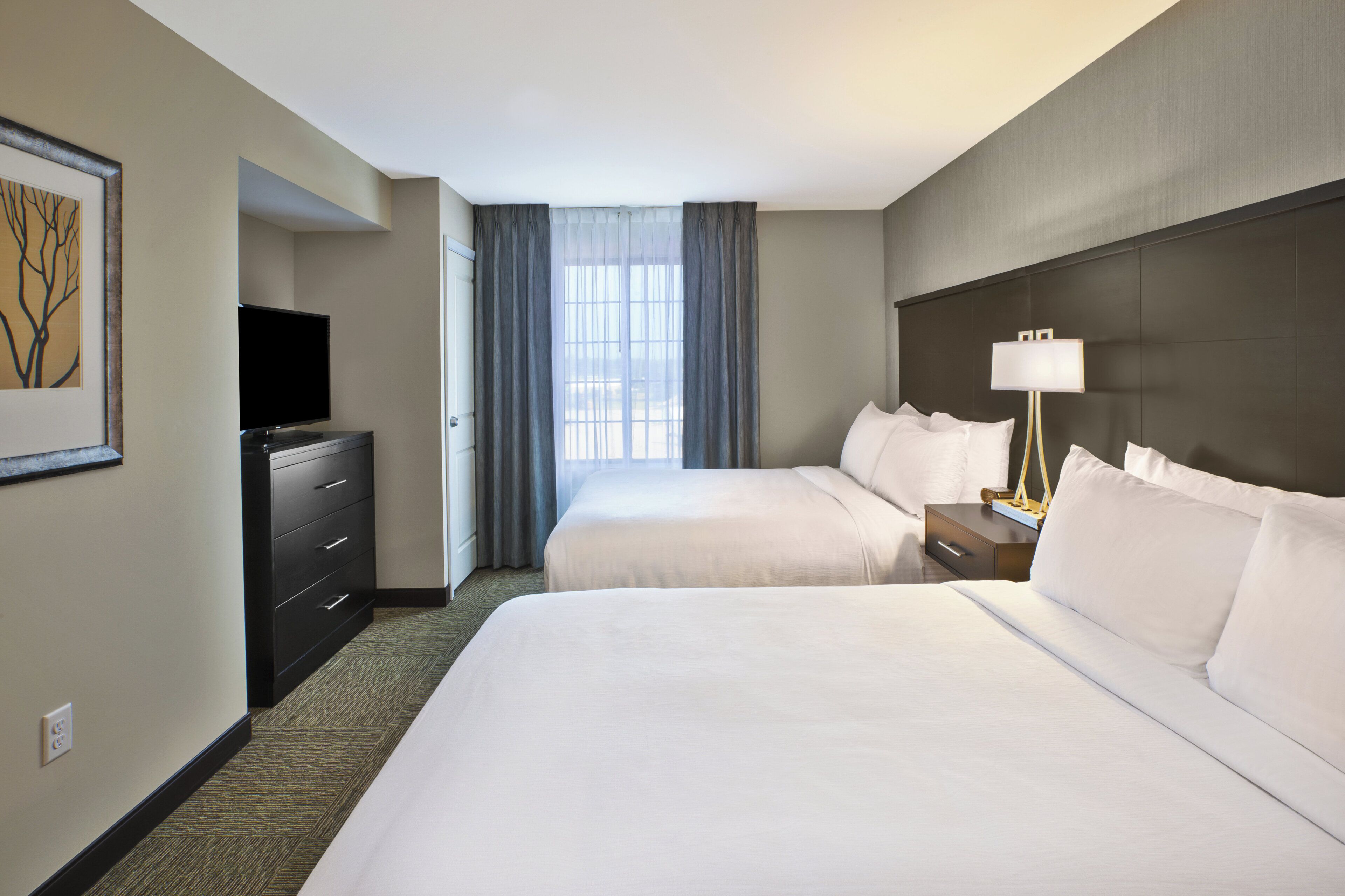 A hotel room with two beds, a TV, a lamp, and a window with curtains.