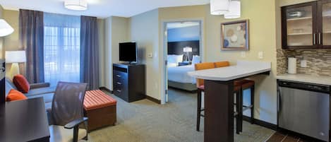 Una habitación de hotel con escritorio, silla, sofá y una zona de kitchenette.