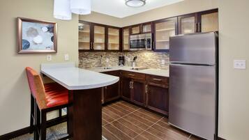 A modern kitchen with a stainless steel refrigerator, a microwave, and a sink. There is a dining area with a chair and a table.