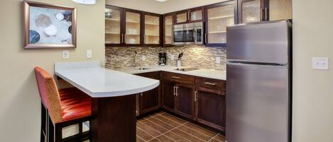 A modern kitchen with a stainless steel refrigerator, a microwave, and a sink. There is a dining area with a chair and a table.