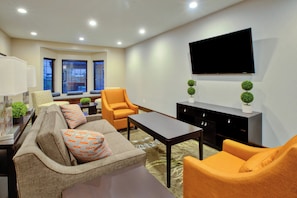 Un salon moderne avec un canapé, des fauteuils, une table basse et un téléviseur à écran plat fixé au mur.