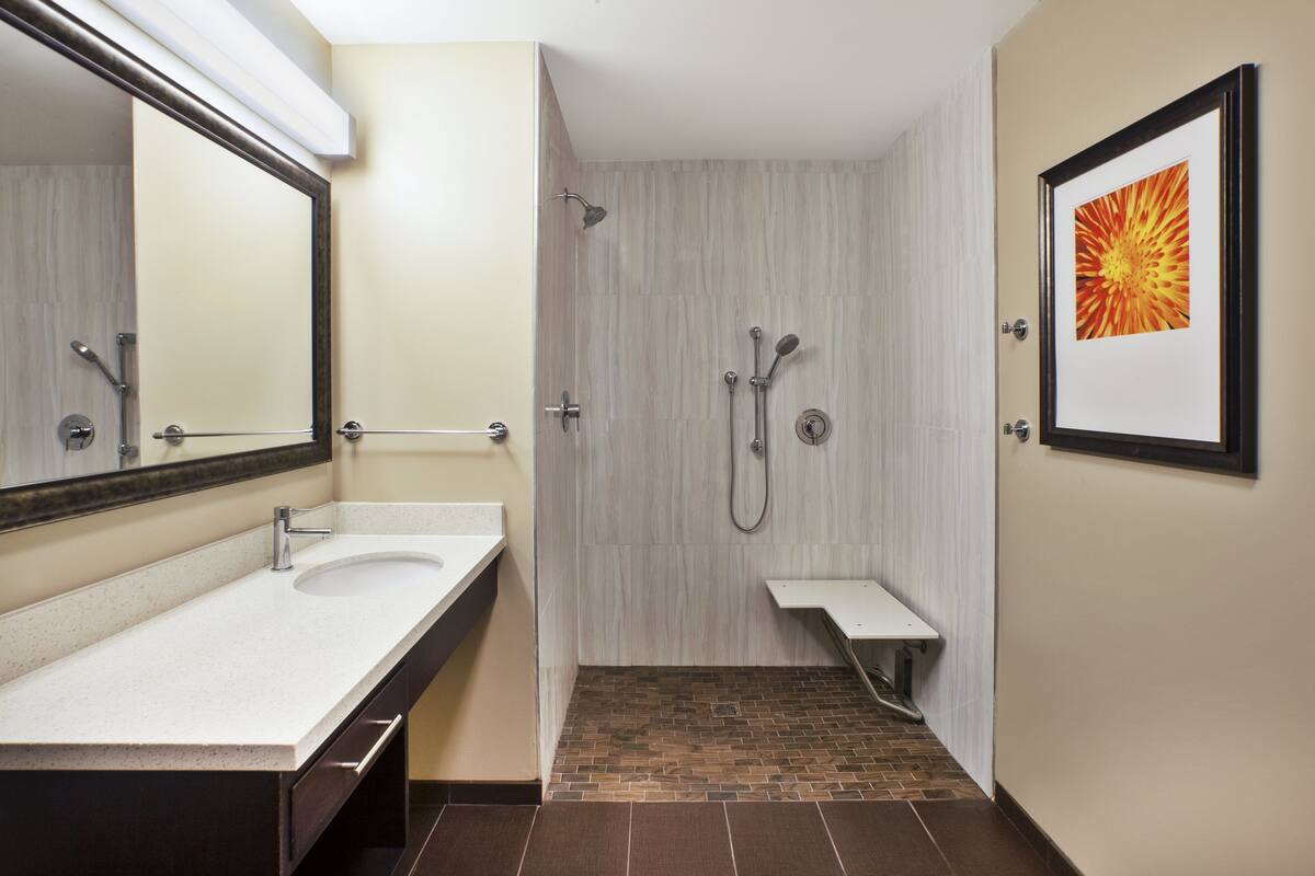 A bathroom with a sink, mirror, shower, and a framed picture on the wall.