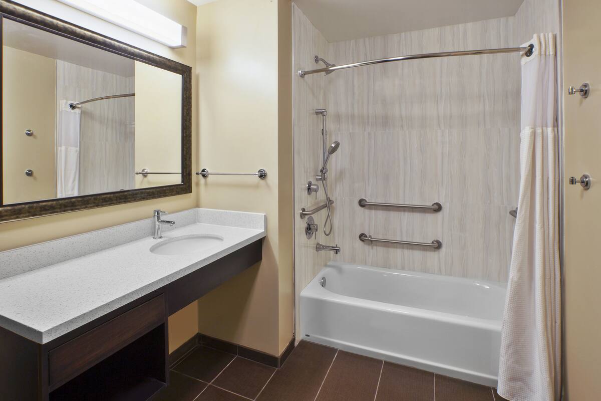 A bathroom with a sink, mirror, and bathtub.