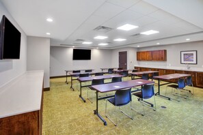 Une salle de conférence équipée de tables et de chaises, d’un écran de projection et d’une porte.