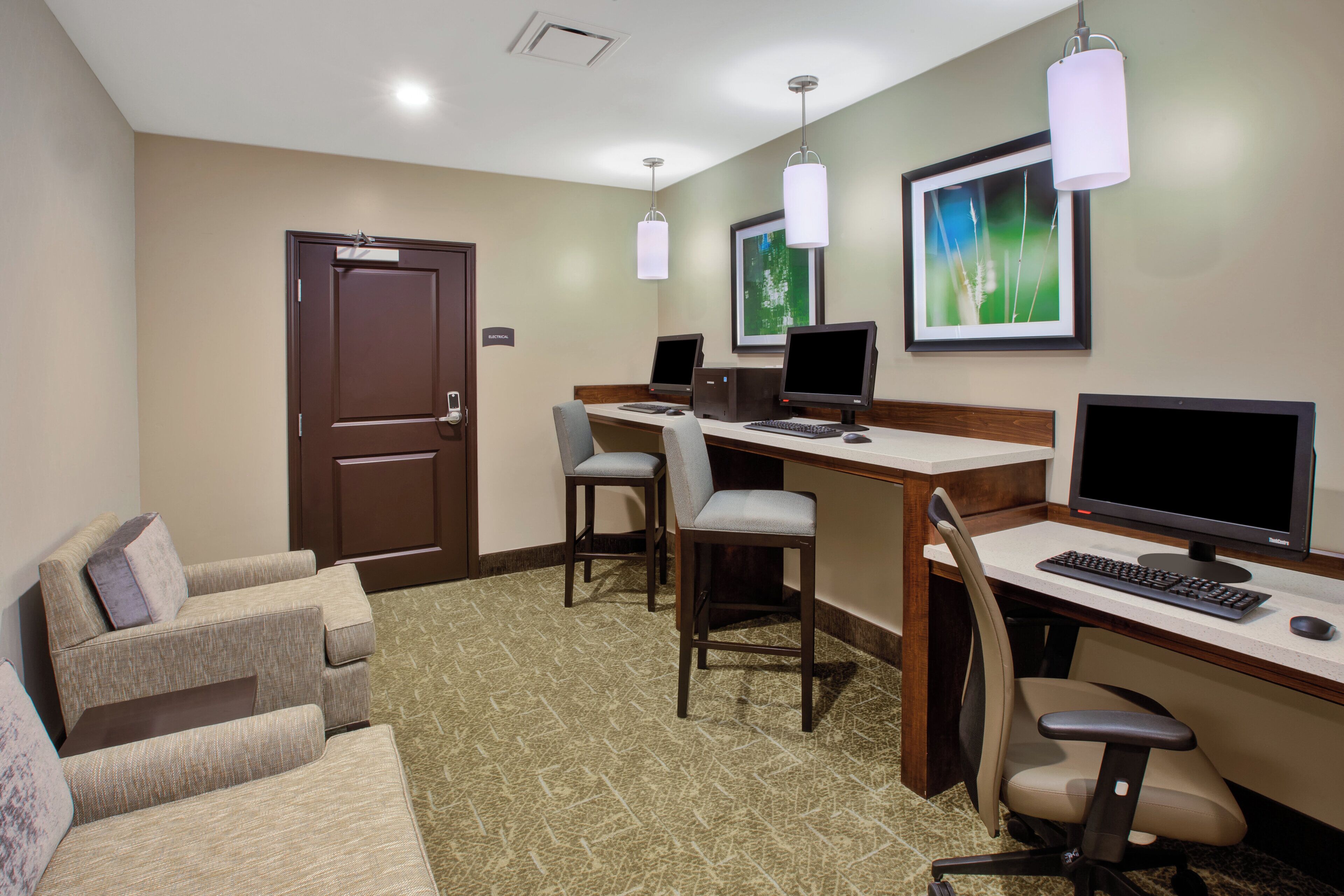 Habitación de hotel con un escritorio, dos monitores de computadora, teclado, ratón, una silla y un sofá.