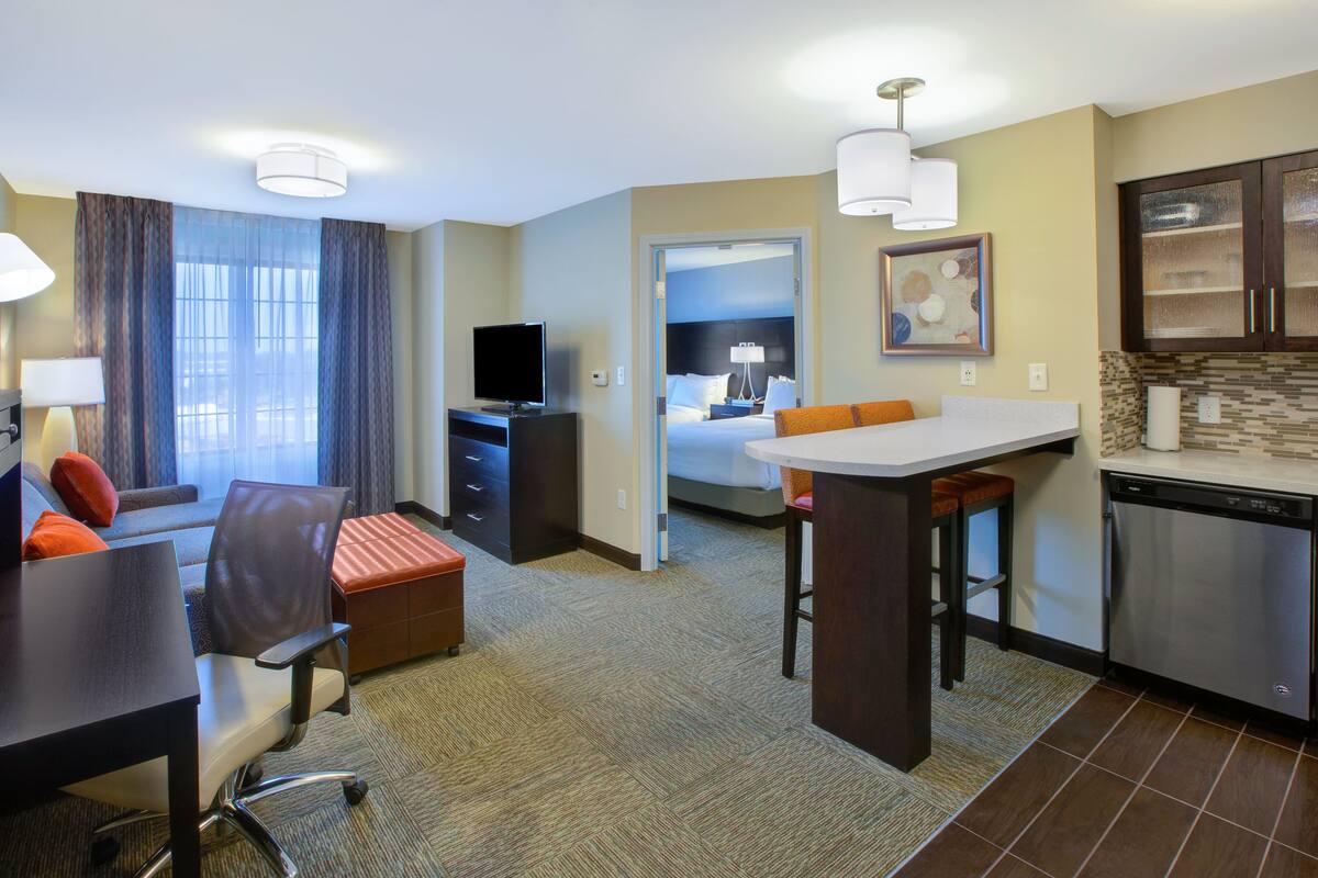 A hotel room with a dining area, a TV, a bed, and a kitchen.