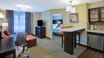 A hotel room with a dining area, a TV, a bed, and a kitchen.