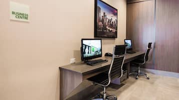 Un centro de negocios con dos estaciones de trabajo de computadora, una silla e imagen de un paisaje urbano en la pared.