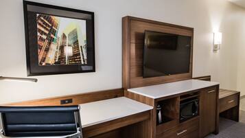 A hotel room with a wooden desk, a flat-screen TV, a framed cityscape photo, and a microwave.