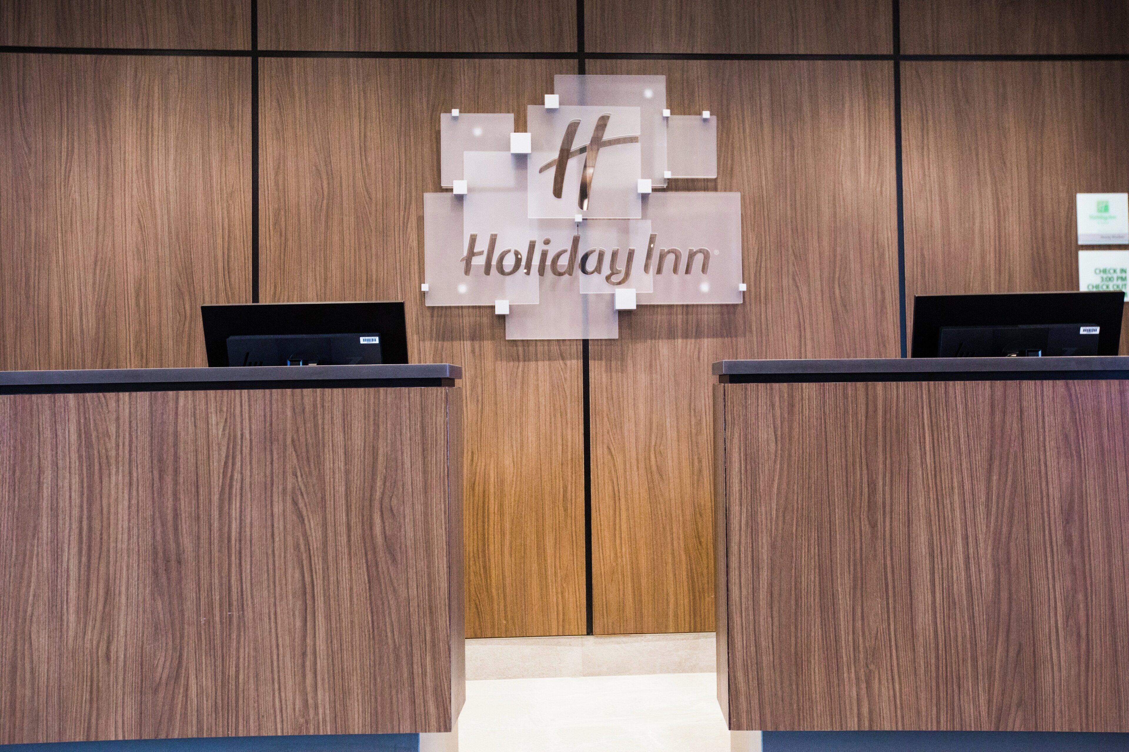 A Holiday Inn reception desk with a wooden panel background and a clear sign above the desk.