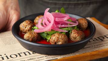 A bowl of meatballs with red onion garnish on a plate.