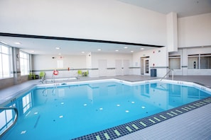 A swimming pool with clear blue water, surrounded by a tiled deck and a few chairs.