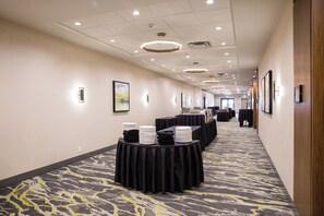 A hotel corridor with tables set up for dining, framed artwork on the walls, and a carpeted floor.