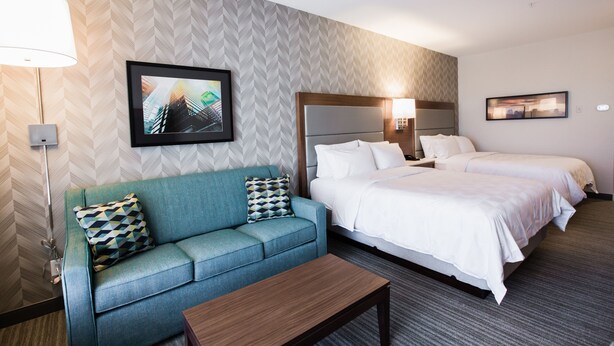 A hotel room with a sofa, two beds, a coffee table, and artwork on the walls. - Holiday Inn Calgary South Conference Center by IHG (Calgary)