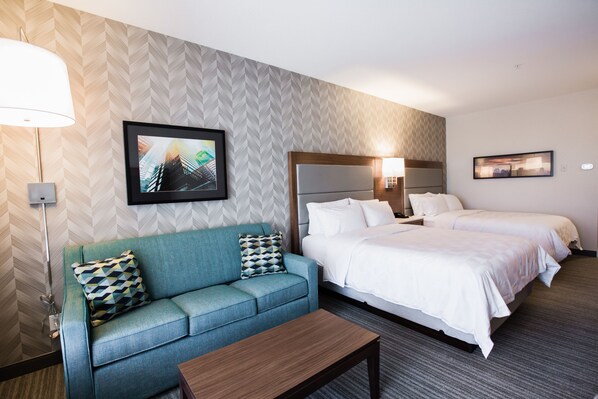 A hotel room with a sofa, two beds, a coffee table, and artwork on the walls. - Holiday Inn Calgary South Conference Center by IHG (Calgary)