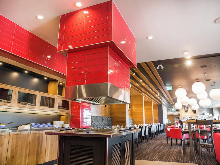 A modern restaurant interior with red accents, wooden paneling, and a central island with kitchen equipment.