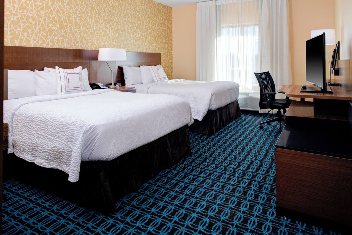 Une chambre d’hôtel avec deux lits, un bureau avec un ordinateur, une chaise et une grande fenêtre avec des rideaux.