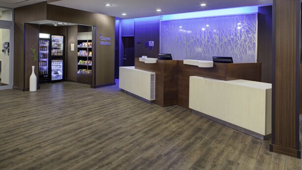 A reception area with a Corner Market refrigerator, a reception desk, and a decorative wall. - Fairfield Inn and Suites by Marriott Detroit Canton (Canton)