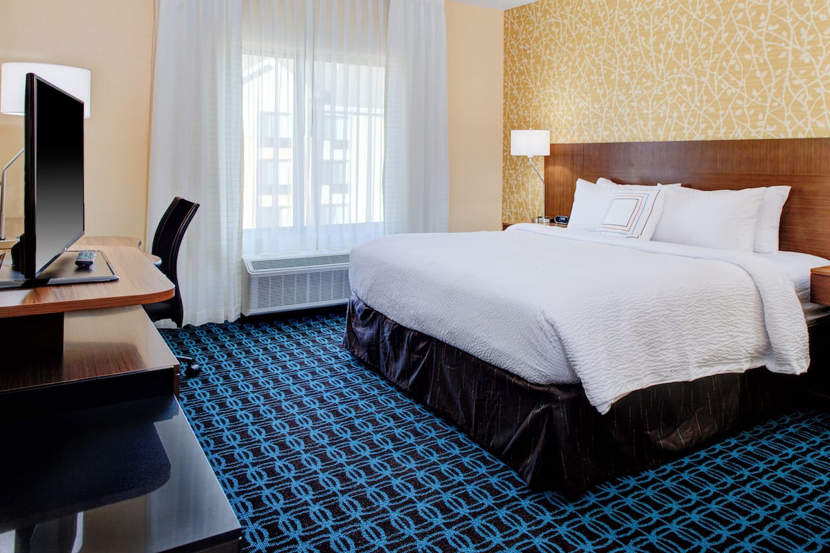 Une chambre d’hôtel comprenant un lit, un bureau avec un ordinateur, une chaise, une fenêtre avec des rideaux et une moquette à motifs.