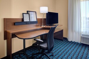 Habitación de hotel con escritorio de madera, una silla de oficina negra, televisor de pantalla plana, estante empotrado con obras de arte enmarcadas y alfombra estampada.