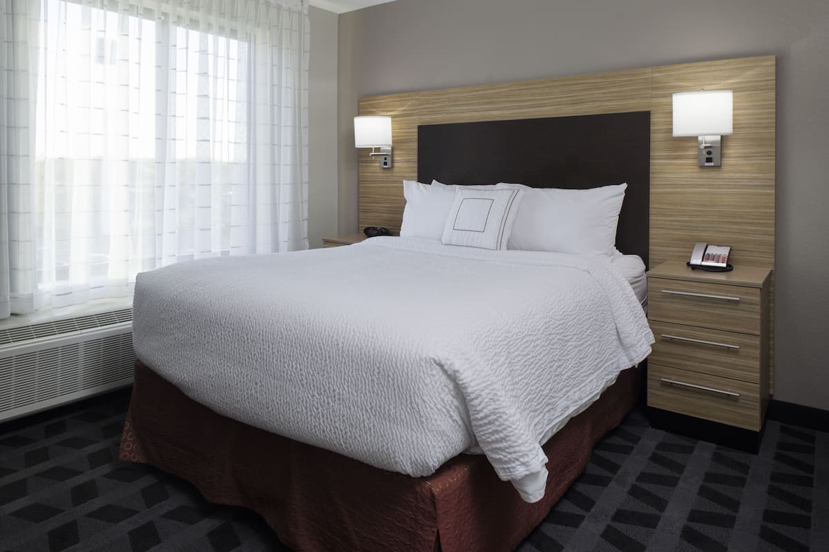 A hotel room with a large bed, two bedside tables with lamps, a heater, and a window with curtains.