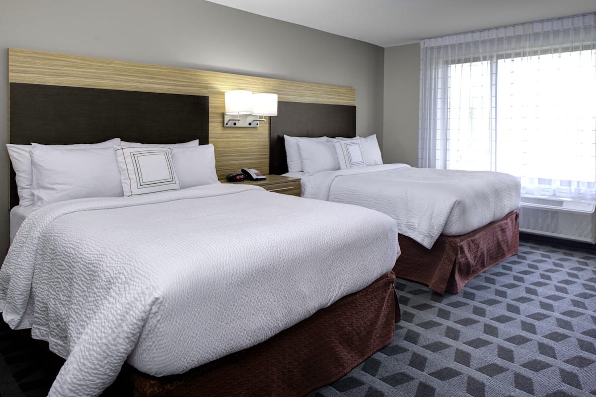A hotel room with two beds, a nightstand with a phone, and a window with curtains.