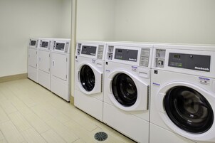 Una hilera de lavadoras blancas y modernas de carga frontal con pantallas digitales, dispuestas en un cuarto de lavado limpio y con baldosas.