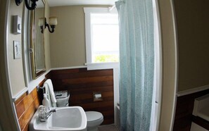 A bathroom with a wooden floor, a white sink, a toilet, and a window with a curtain. - Leigh Lani Guest House (Victoria)