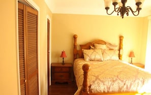 A bedroom with a wooden bed, two bedside tables with lamps, and a chandelier. - Leigh Lani Guest House (Victoria)