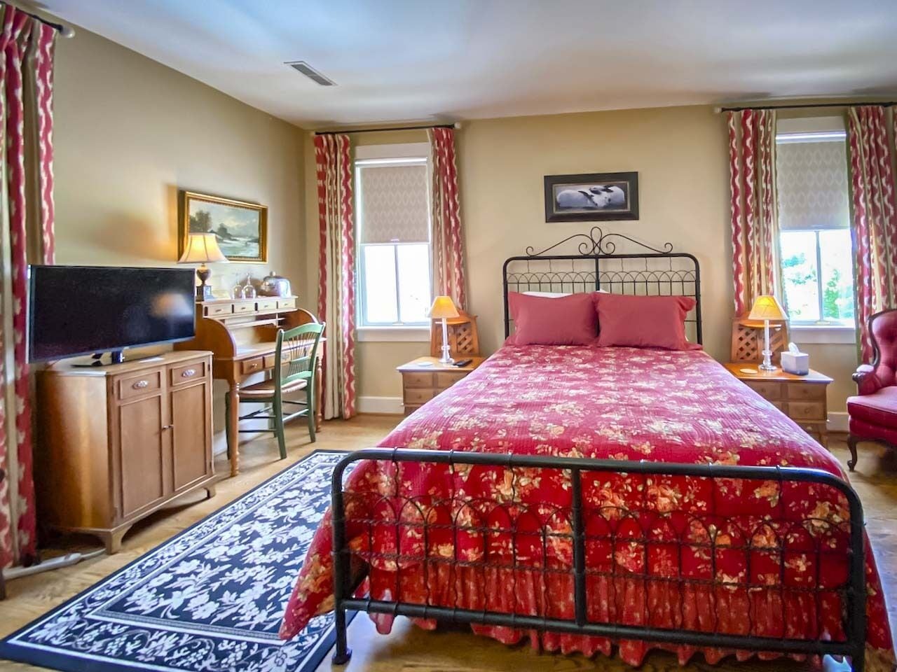 A bedroom with a bed, a desk, a chair, a television, and a window with curtains.